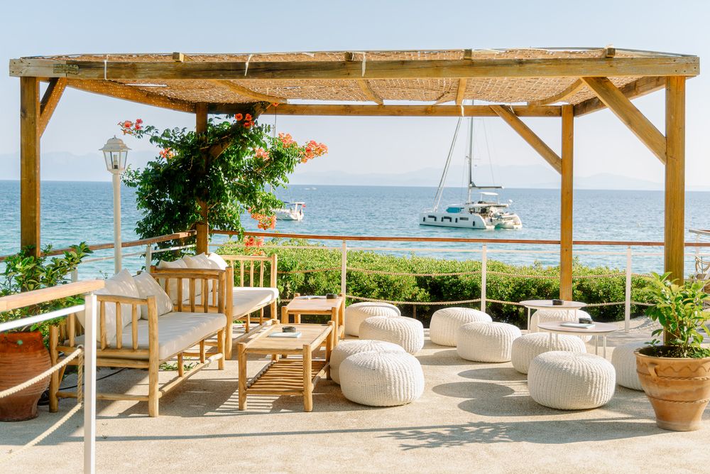 Outdoor lounge with wooden pergola, soft seating, and sea view.