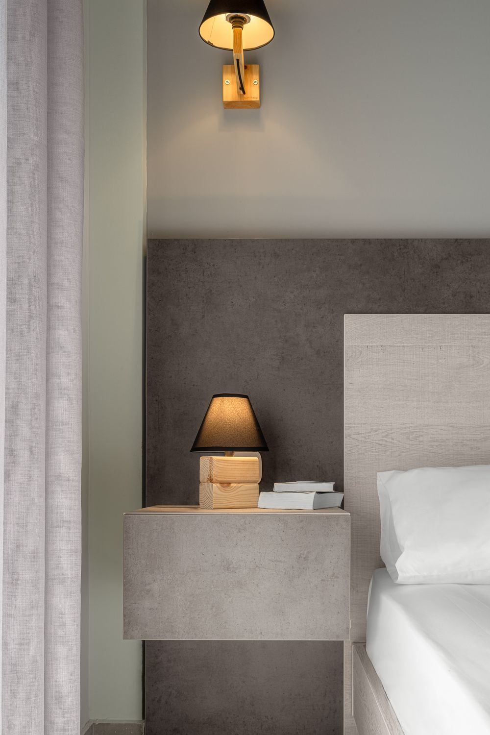 Minimal bedside table with a warm-lit lamp beside a soft, neutral-toned bed in a modern interior.