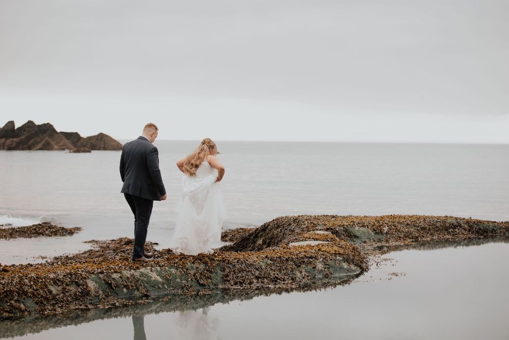 Wedding couple share romantic moment on rocky seashore with ocean backdrop and tidal reflection.