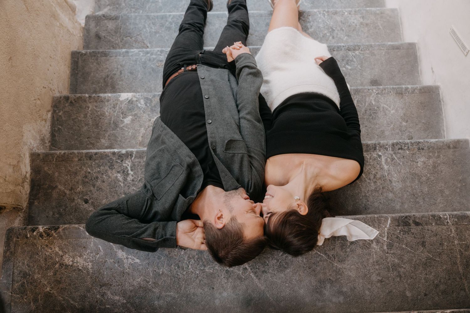 Two people lying together on concrete steps wearing casual clothing in an intimate pose.