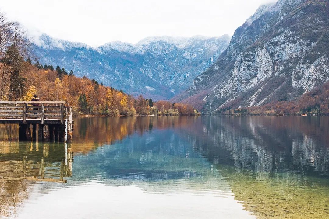 Autumn mountain landscape reflected in a calm lake with a wooden boathouse on the shore.
