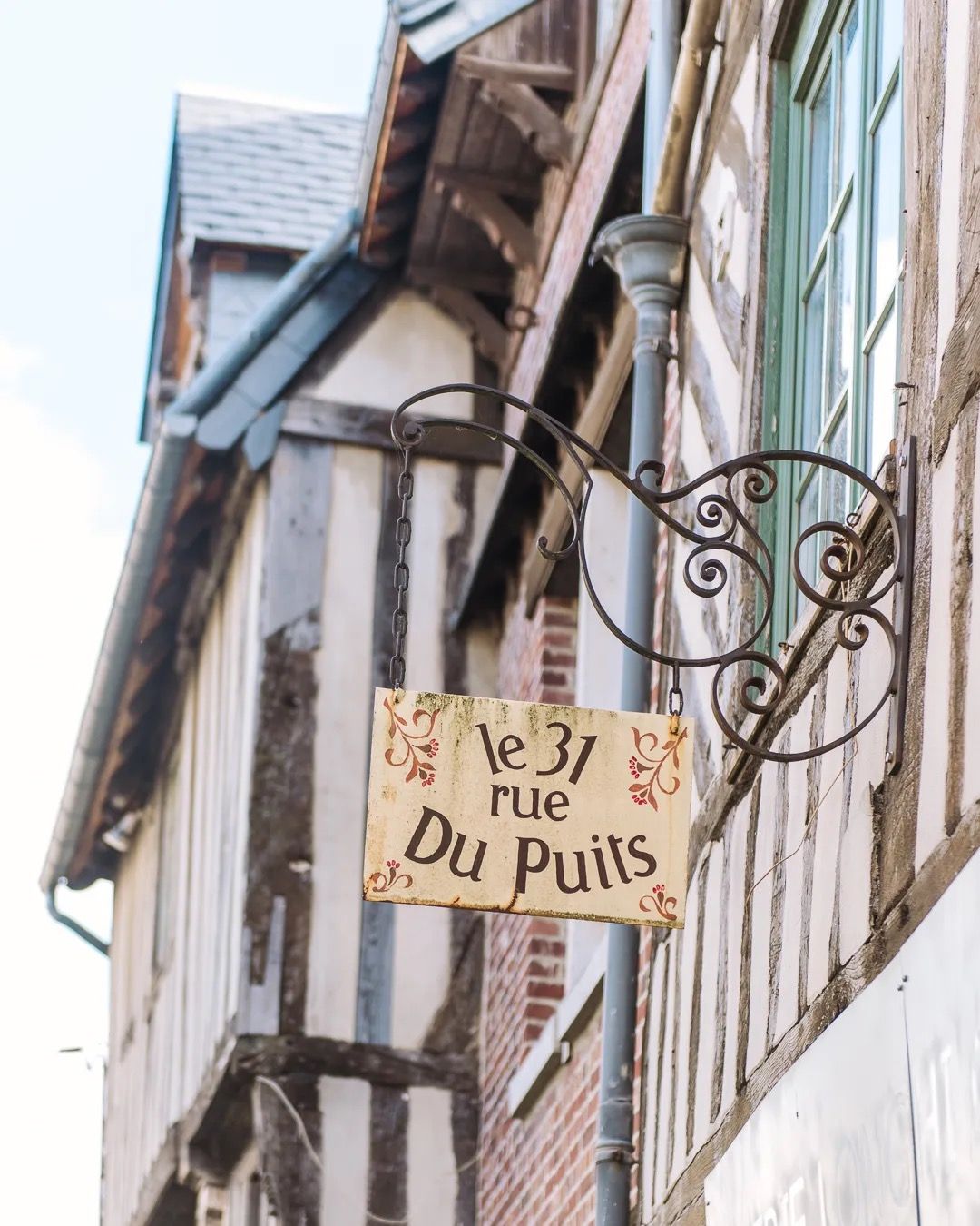 Vintage pub sign hanging from a timber-frame building in a historic French town.