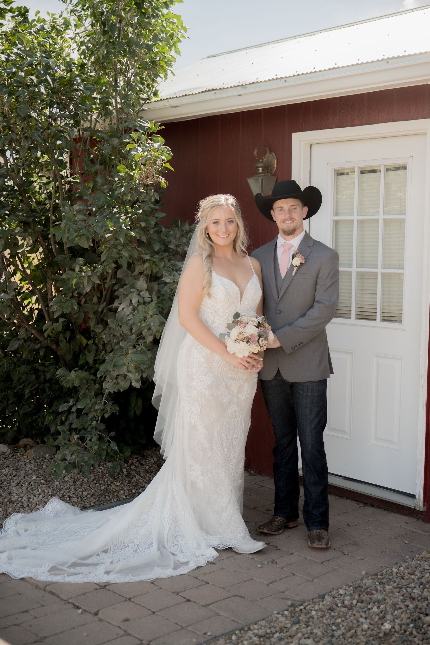 A couple poses together on their wedding day outside a red building with a white door.