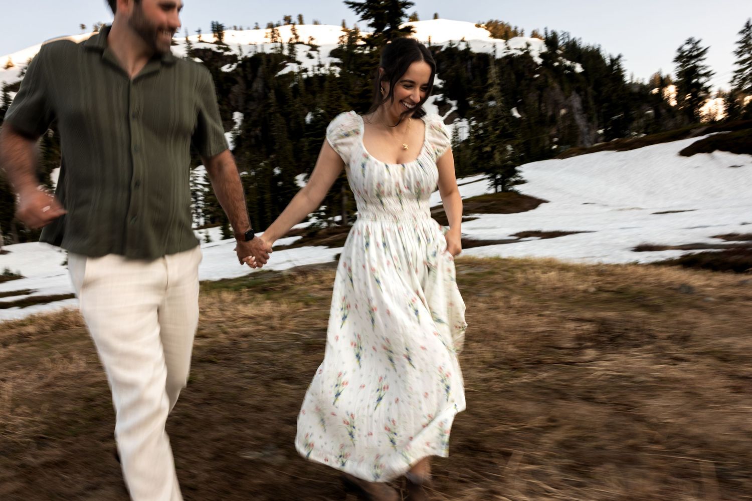 A couple in wedding attire dances joyfully together in a rustic outdoor setting at sunset.