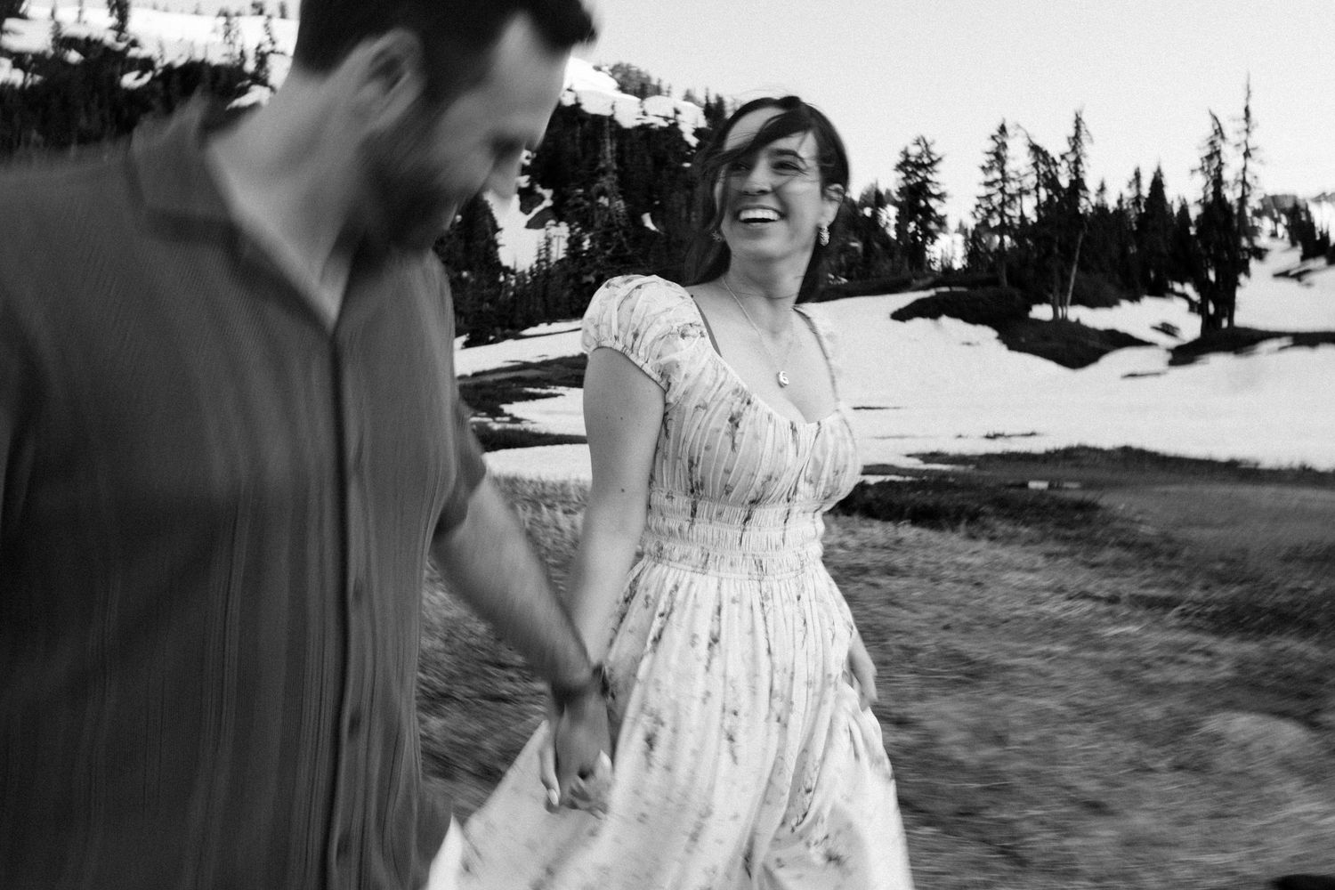 A black and white photo captures a couple dancing together in a mountain setting with snow patches visible.