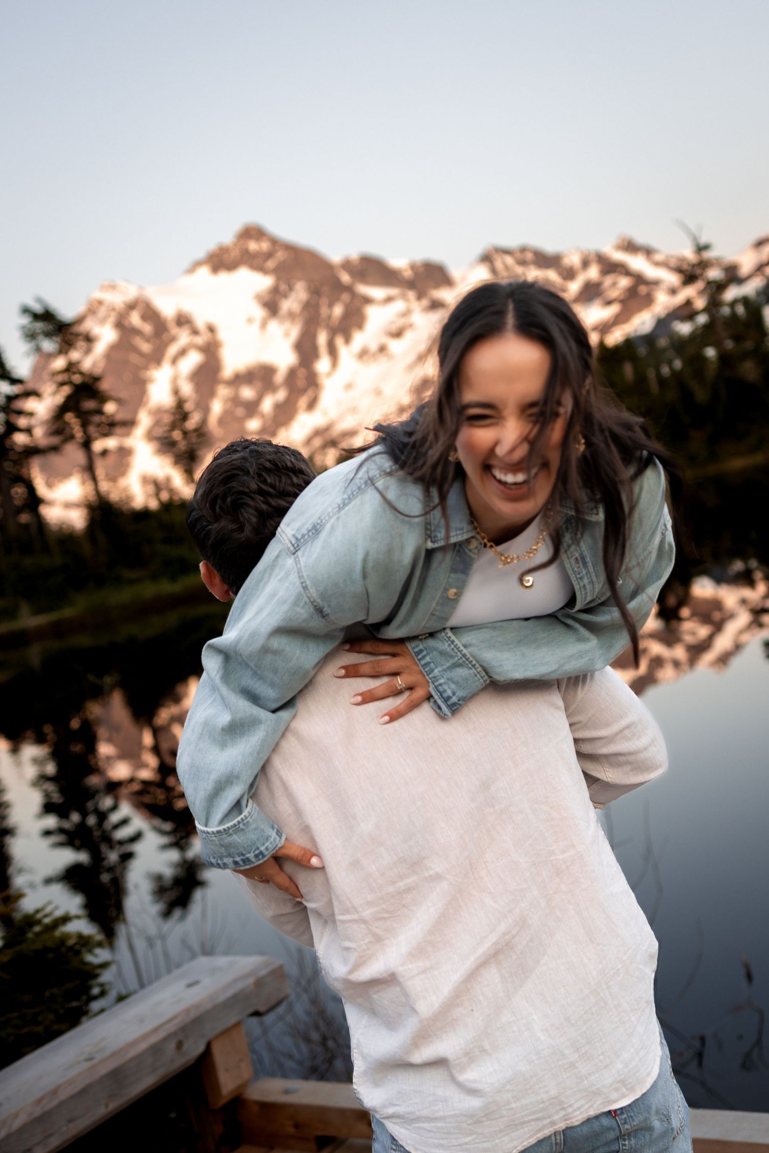 Candid moments of laughter and joy captured at sunset by a lake with mountains in the background.