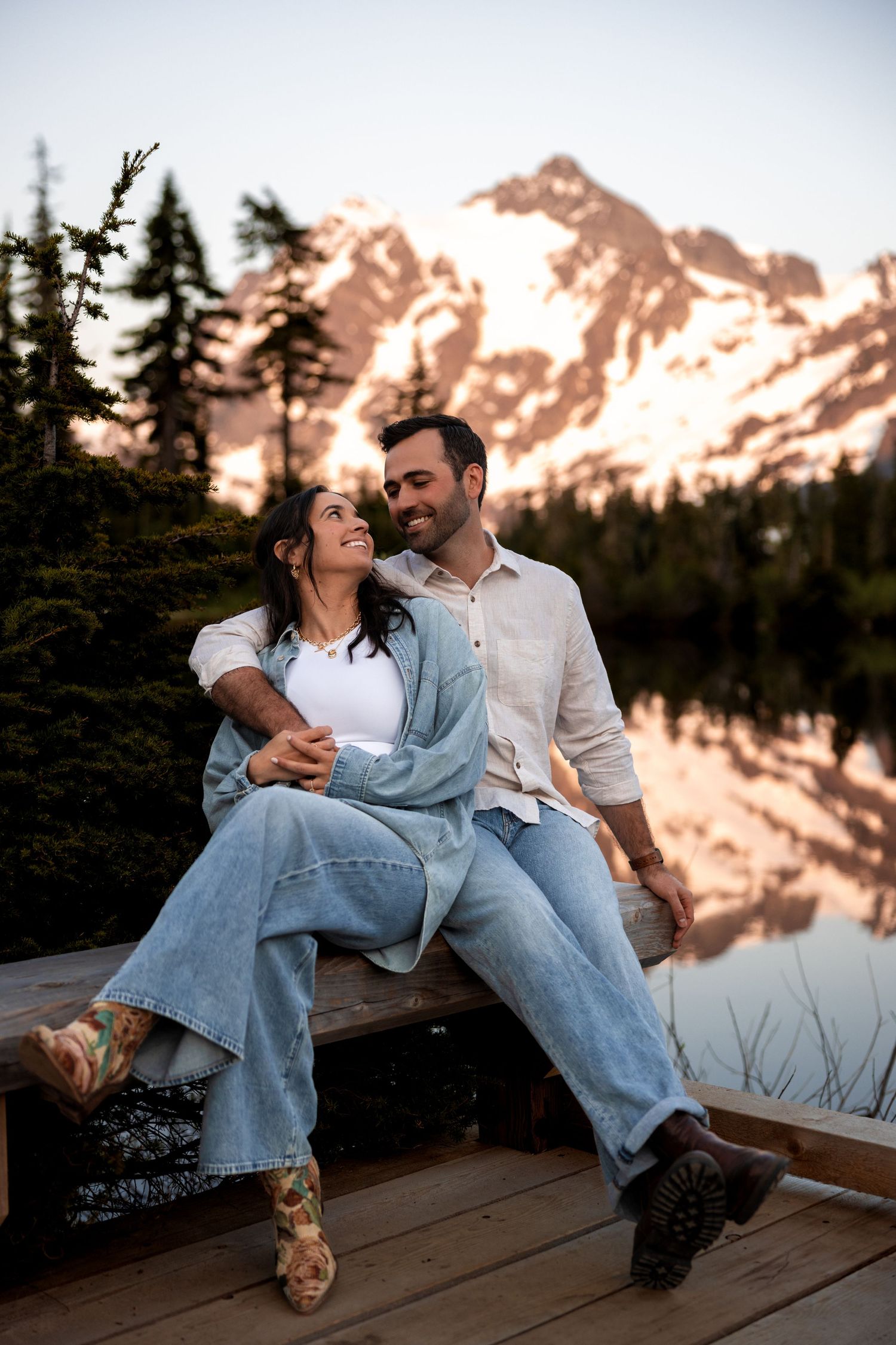 A couple relaxes on a wooden dock while enjoying mountain views during golden hour.