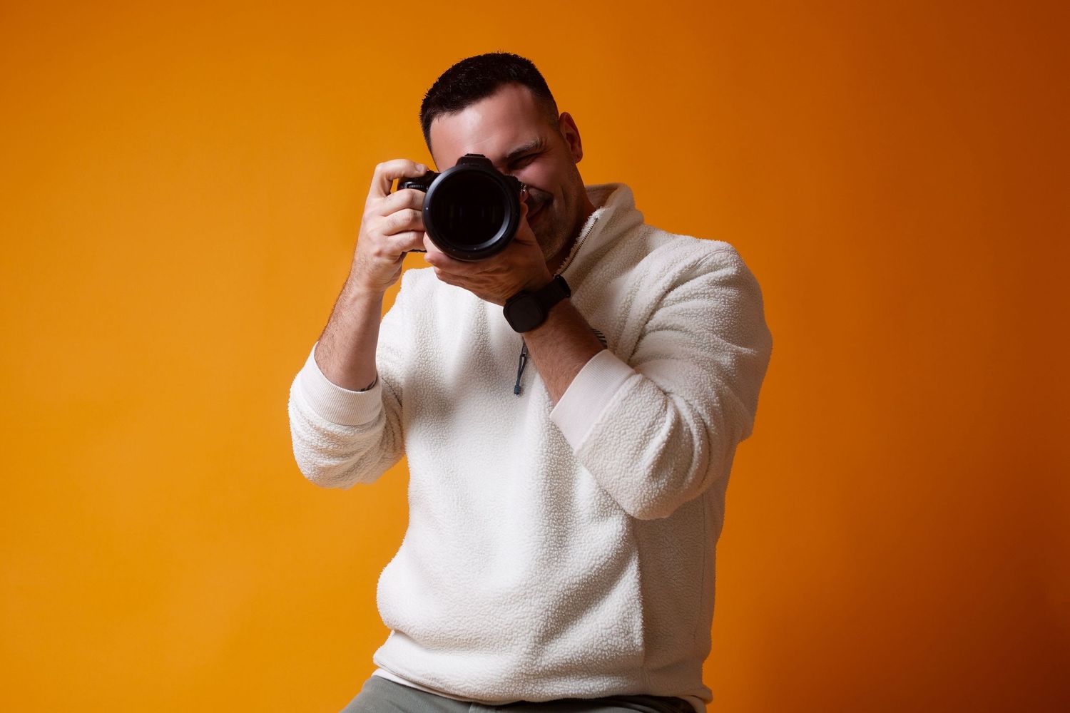 Photographer in white sweater takes photos against vibrant orange background in sequence of progressive shots.
