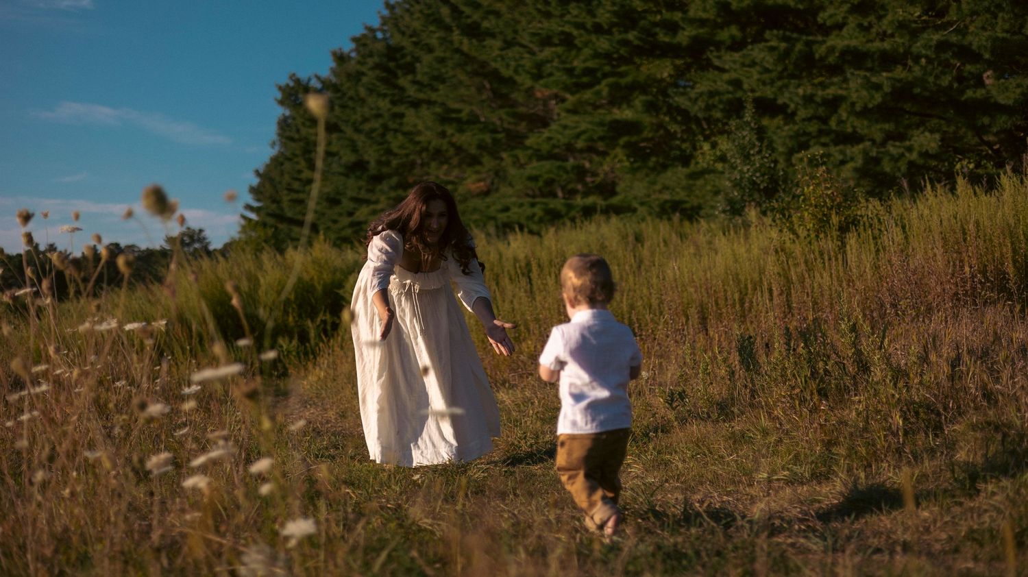 A couple walks through a scenic coastal trail with tall grass and blue sky on a sunny summer day.
