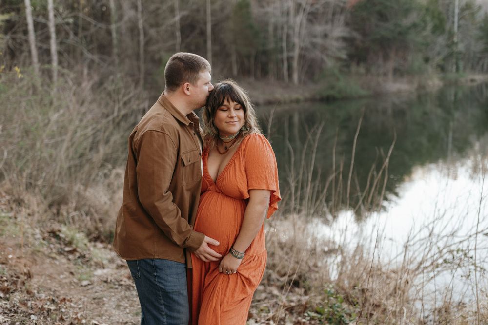 Couple in autumn tones pose for maternity photos beside a serene lake. Virginia/ North Carolina Maternity Session