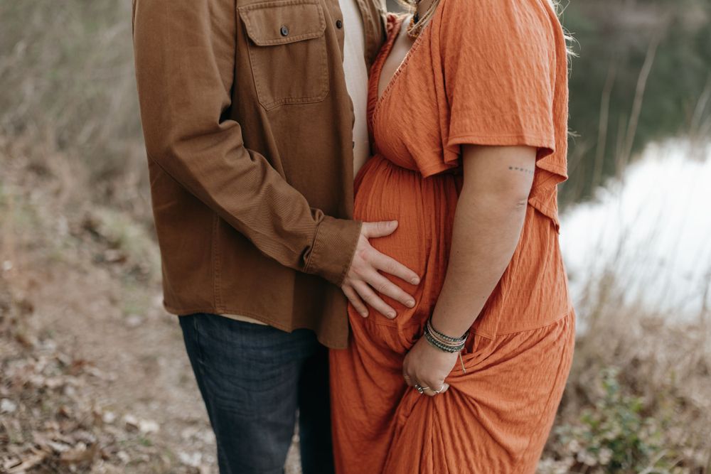 Close-up shot of hands tenderly cradling a pregnant belly in an outdoor setting. Virginia/ North Carolina Maternity Session