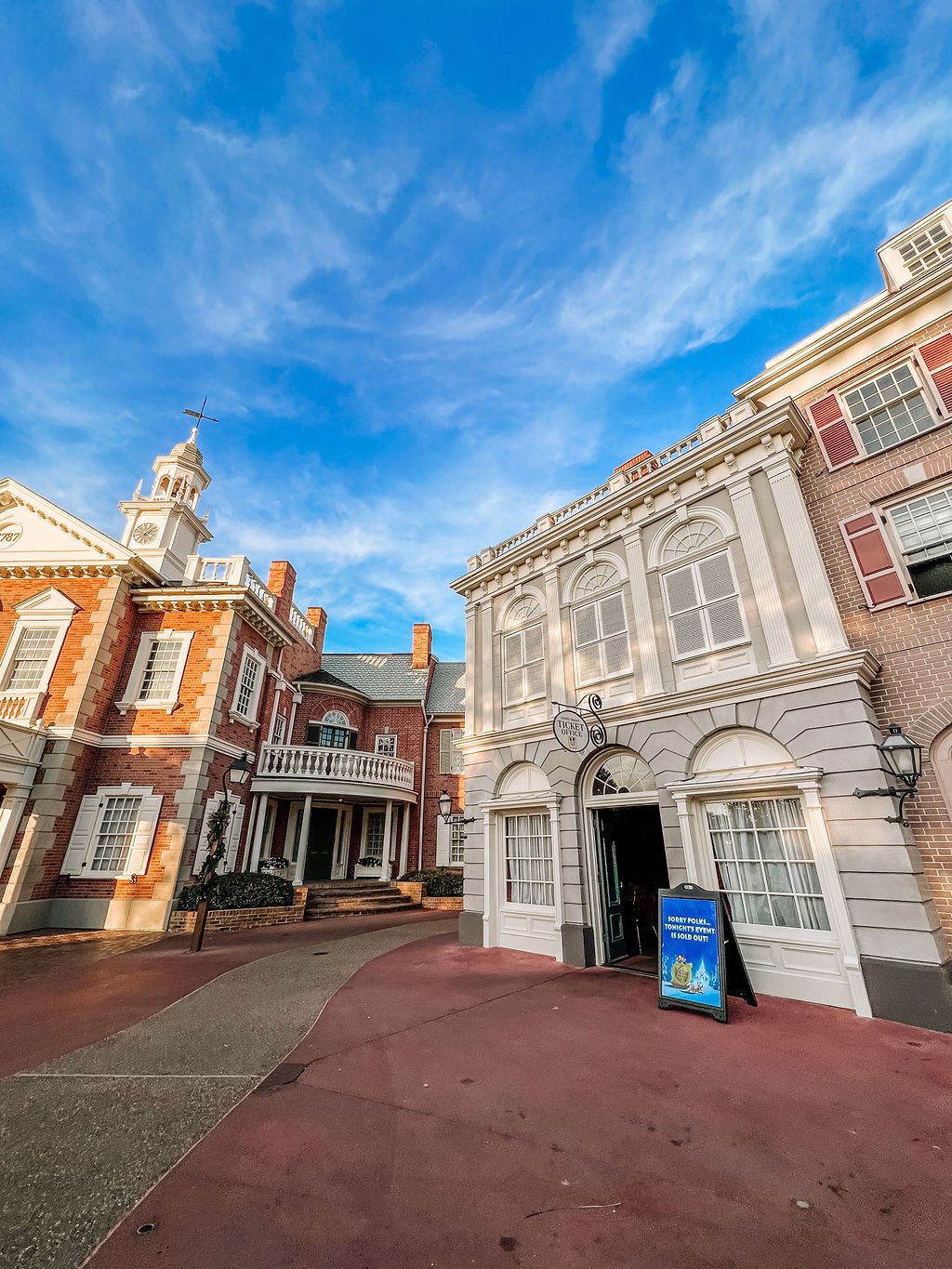 Colonial style architecture with red brick and white trim buildings under bright blue skies at Disney's Liberty Square.