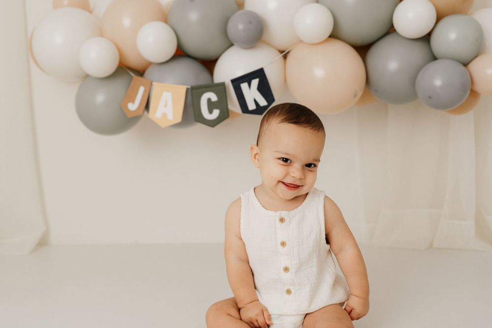 Festive first birthday setup with balloons and banner in neutral colors.