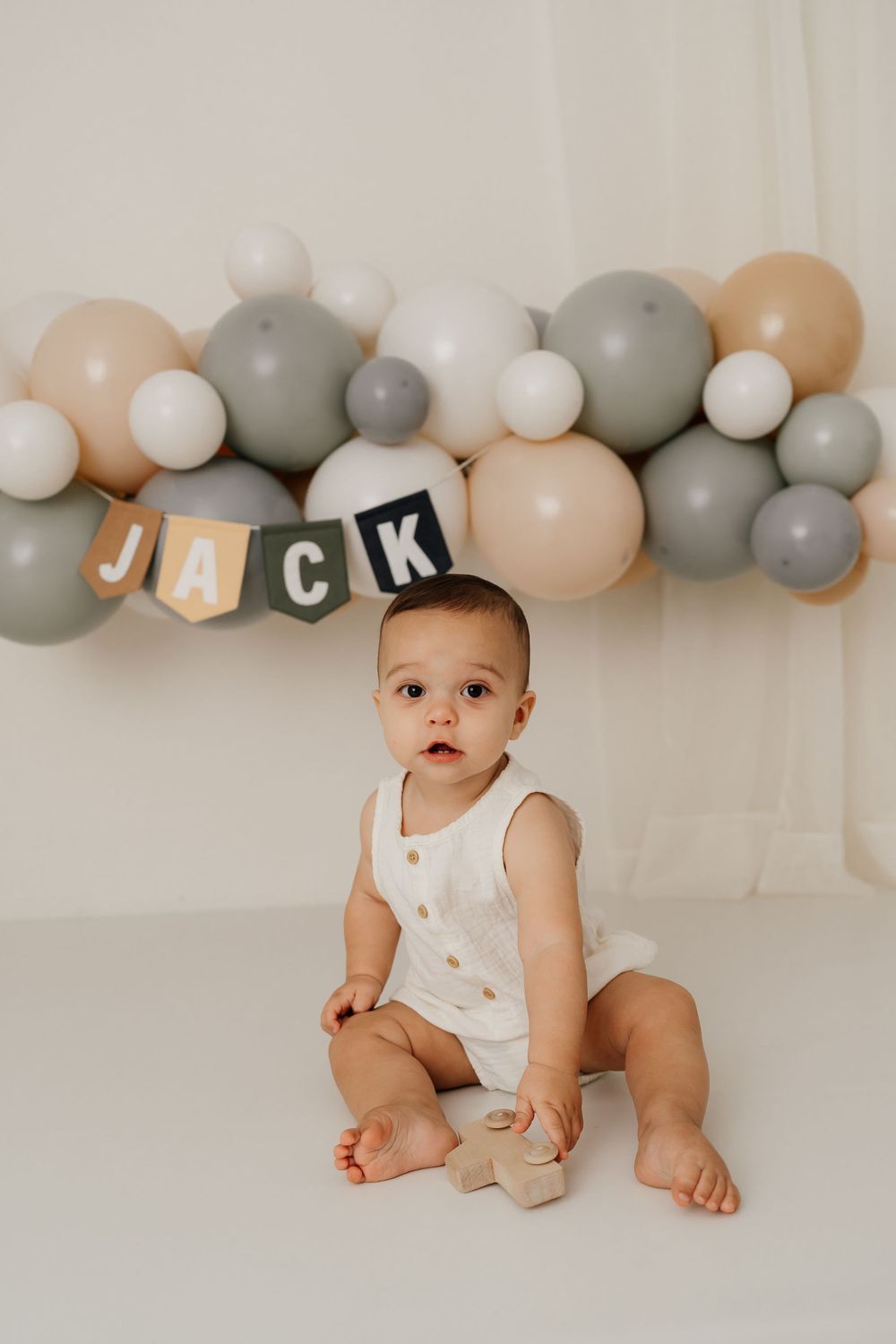 Birthday celebration scene with balloon arch and banner in soft gray and peach tones.