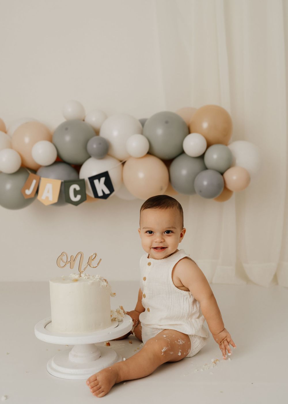 Birthday setup with white cake and balloon decoration in muted pastel colors.