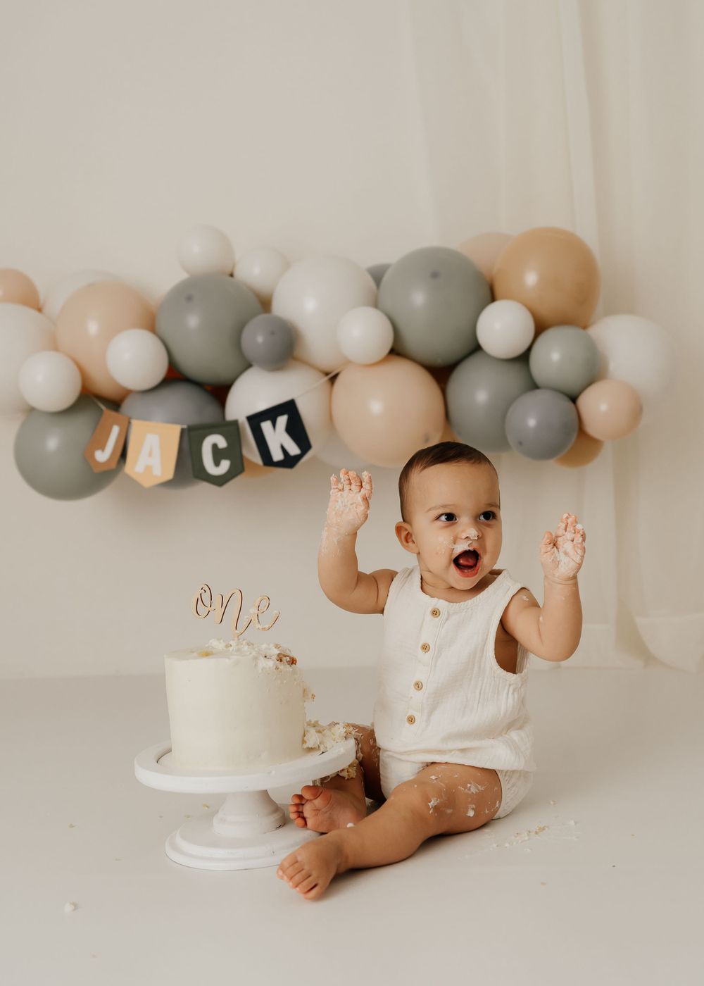 Celebratory moment with white birthday cake and balloon arch in neutral tones.