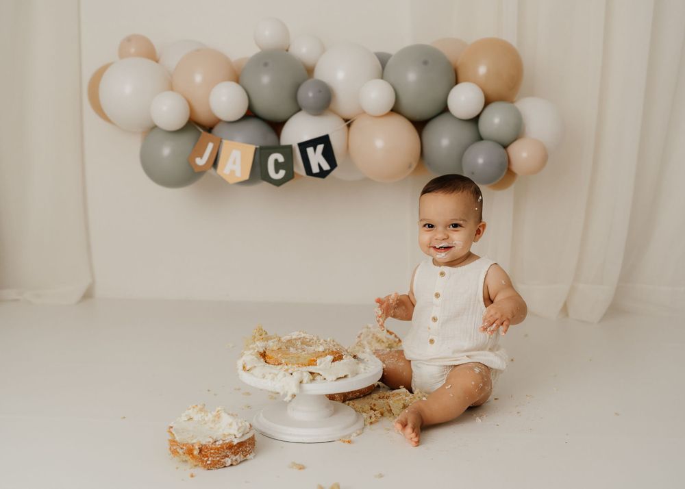 Birthday celebration with smashed cake and balloon decorations in soft colors.