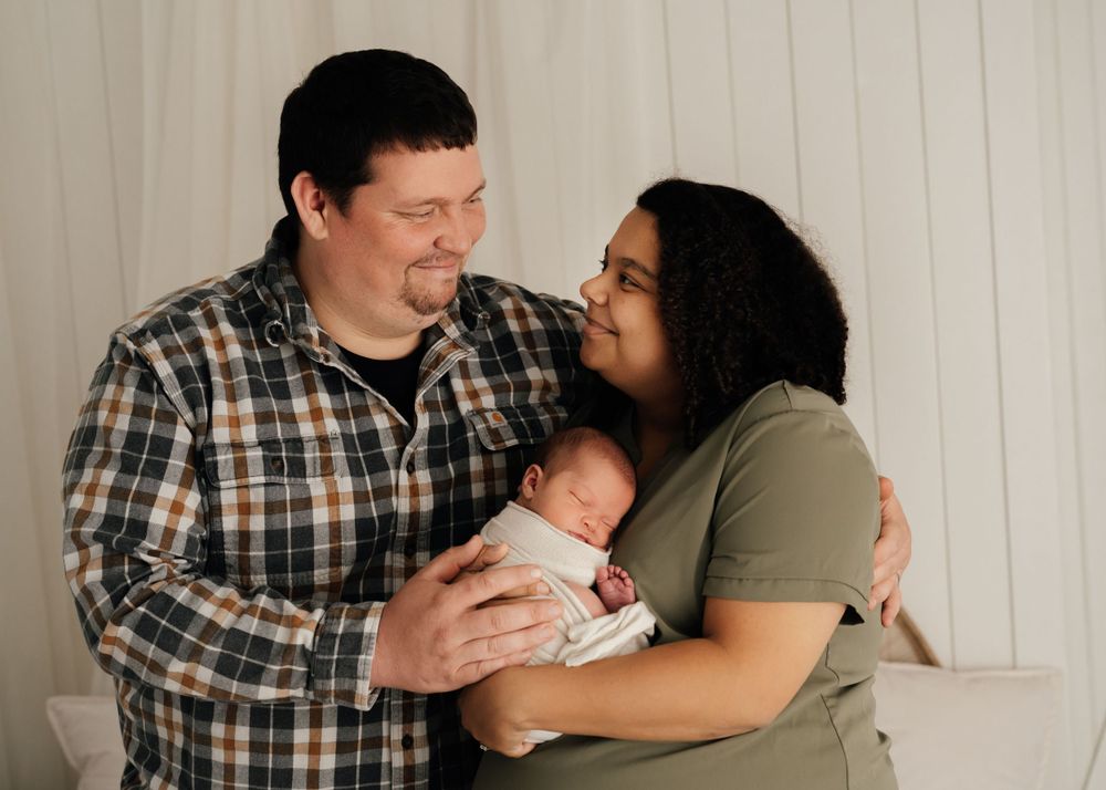 Family shares intimate moment together during newborn photoshoot against white backdrop.