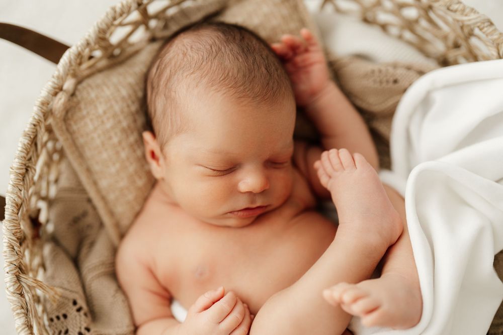 Sleeping newborn nestled in textured basket with white linens.