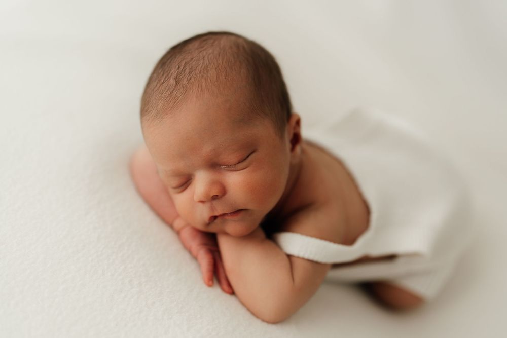 Peaceful sleeping newborn rests on white backdrop in professional portrait.