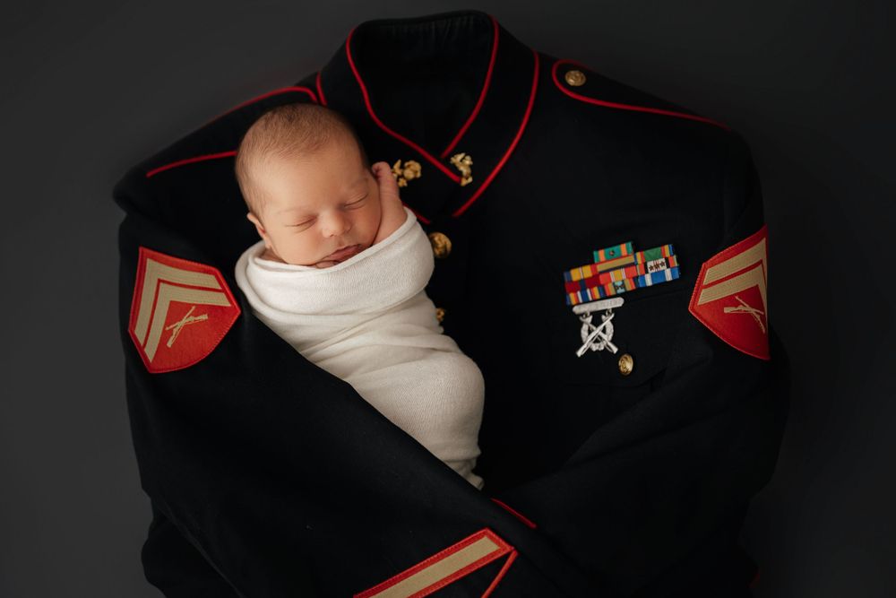 Newborn wrapped in white swaddle rests on decorated Marine Corps dress uniform.