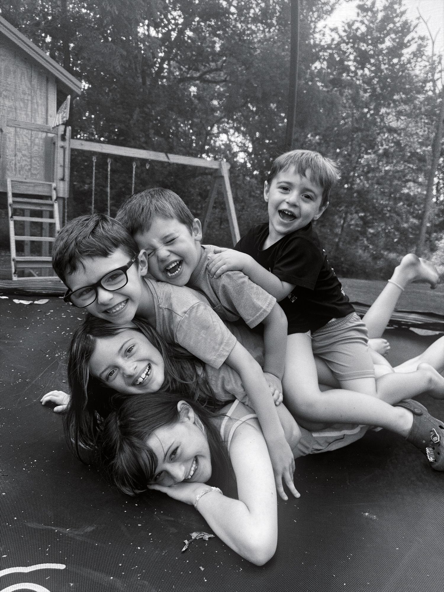 Children sit together on a wooden bench under a large tree on a scenic hillside during a sunny afternoon.