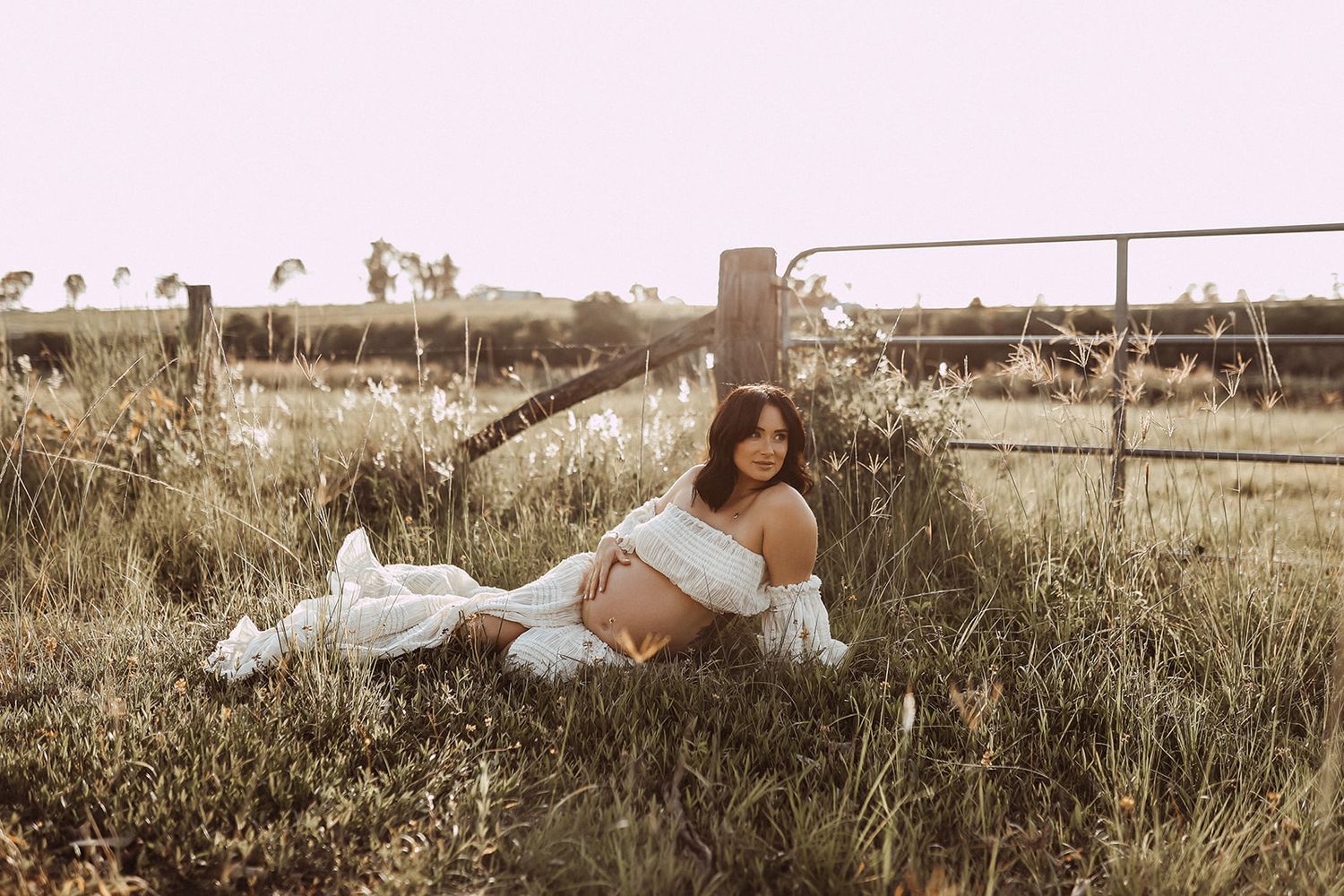 Woman in white crop top lying in grass field during sunset photoshoot.