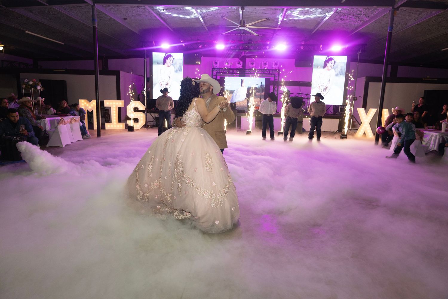 Wedding couple dancing their first dance on a misty dance floor with purple lighting and digital screens in the background.