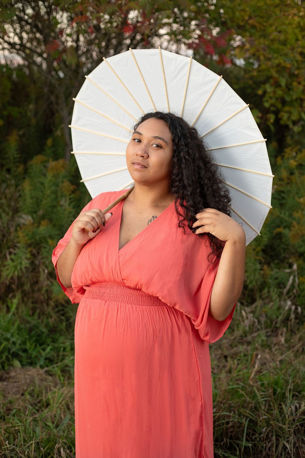 Portrait of woman with white parasol in flowing coral dress during sunset.