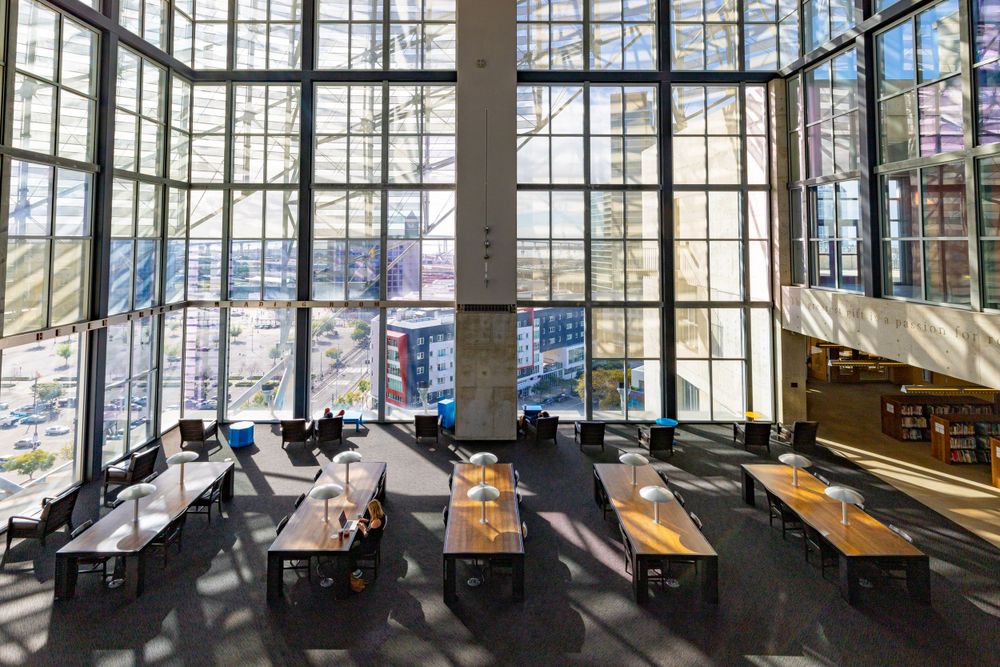Modern reading space at the San Diego Public Library with large windows, wooden tables, and industrial ceiling design.