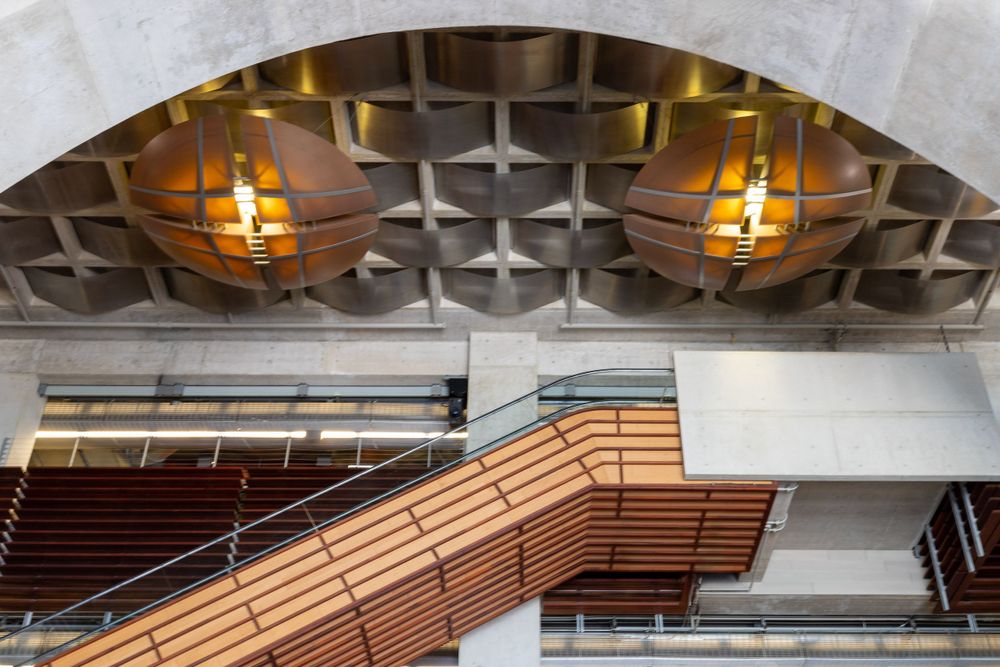 Interior architectural detail of San Diego Public Library showing wooden stairs and geometric ceiling with pendant lighting.
