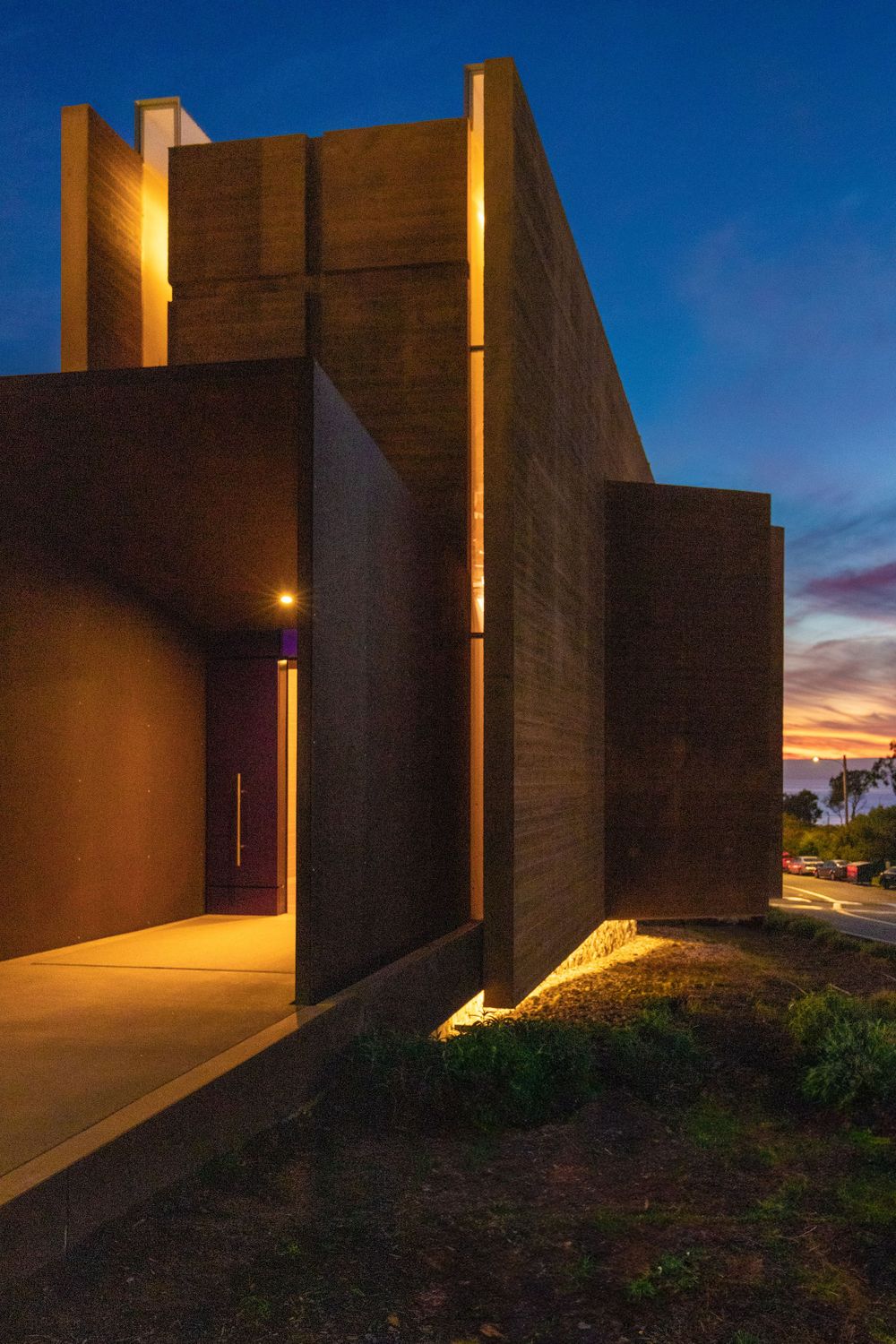 Modern concrete building exterior illuminated at dusk with dramatic lighting and shadows.