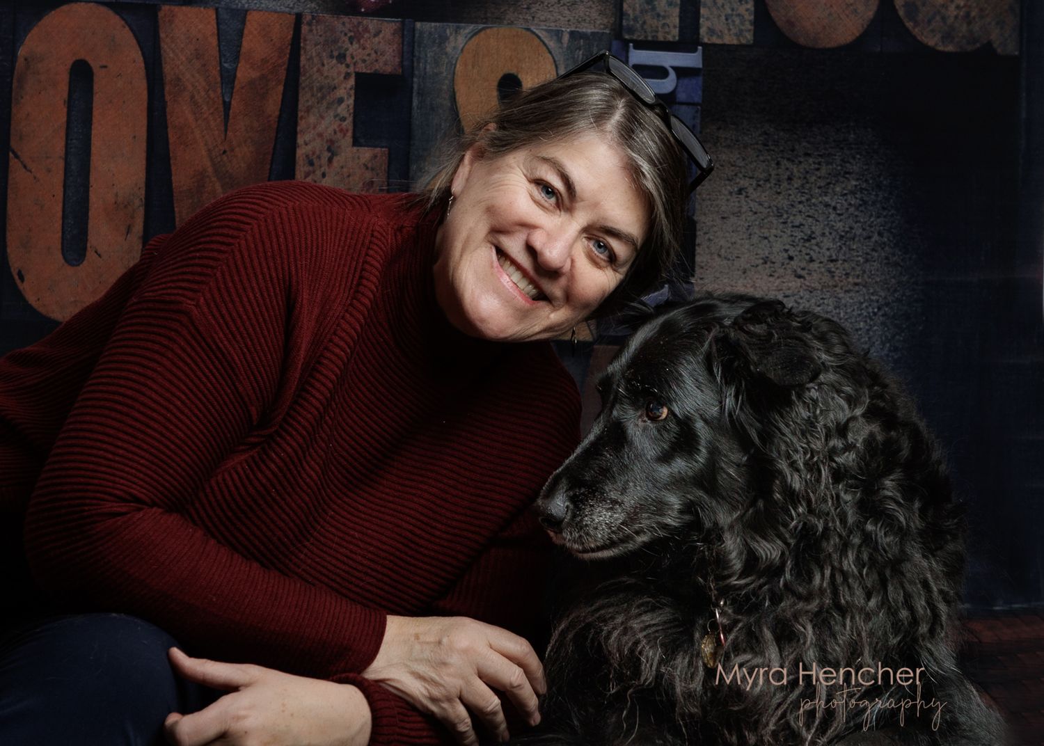 Black dog with curly fur poses with companion in front of dark background with text.