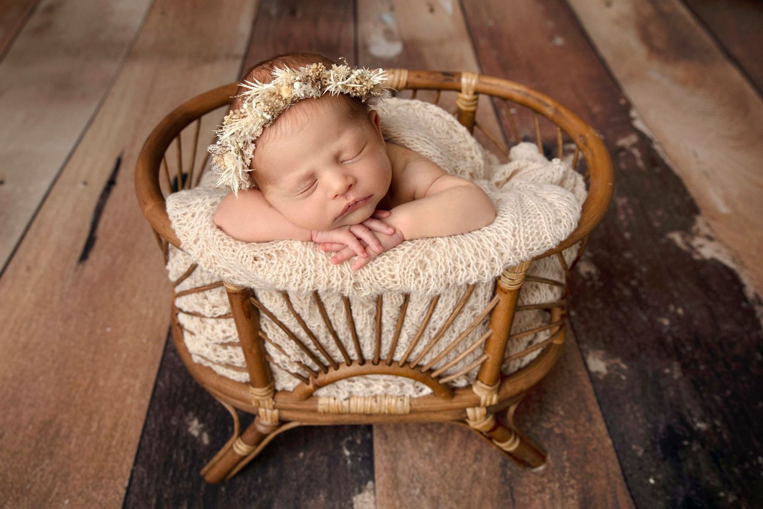 Newborn baby sleeping peacefully in vintage wicker bassinet with cream bedding.