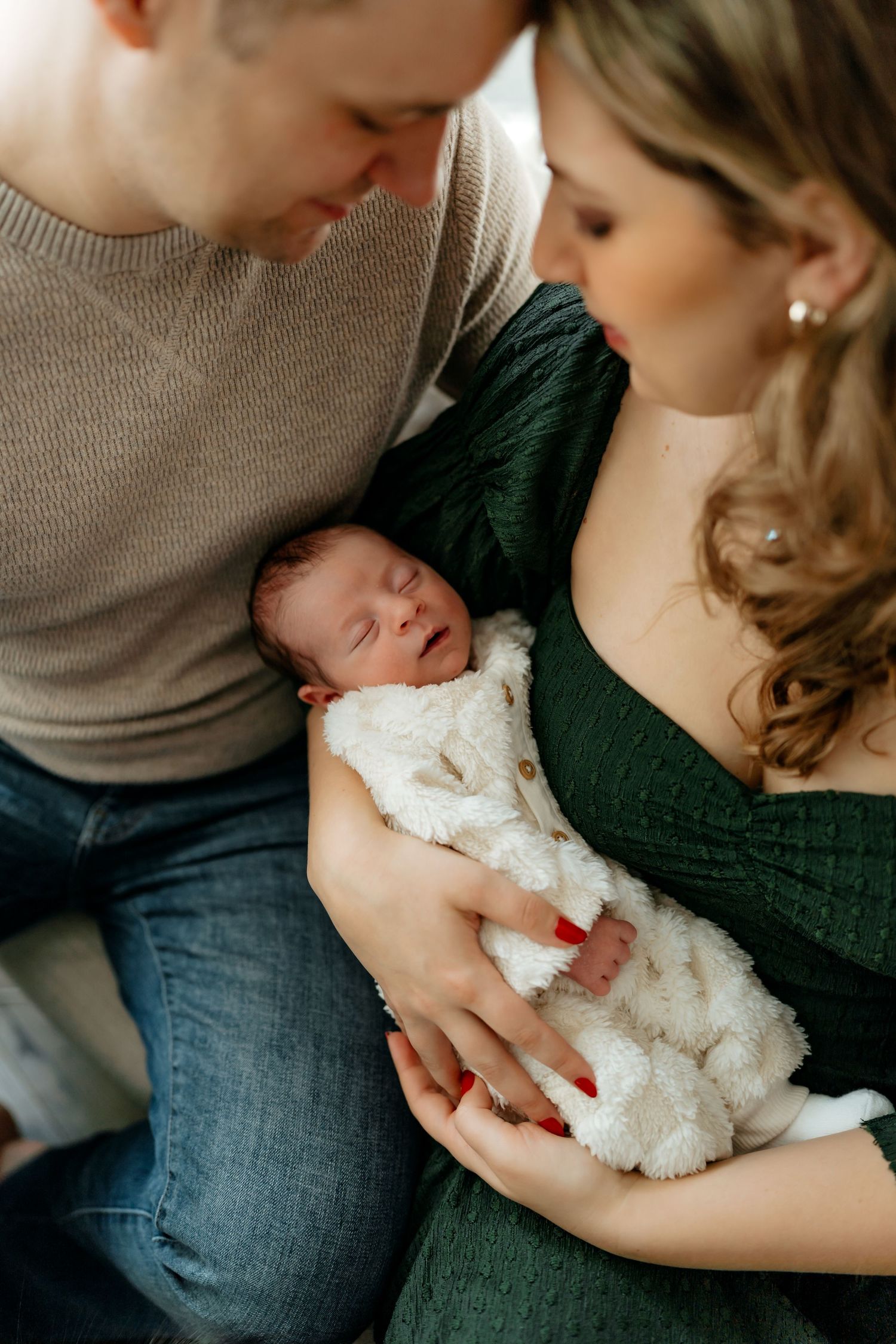 A tender family moment with parents looking down at their newborn wrapped in a white blanket.
