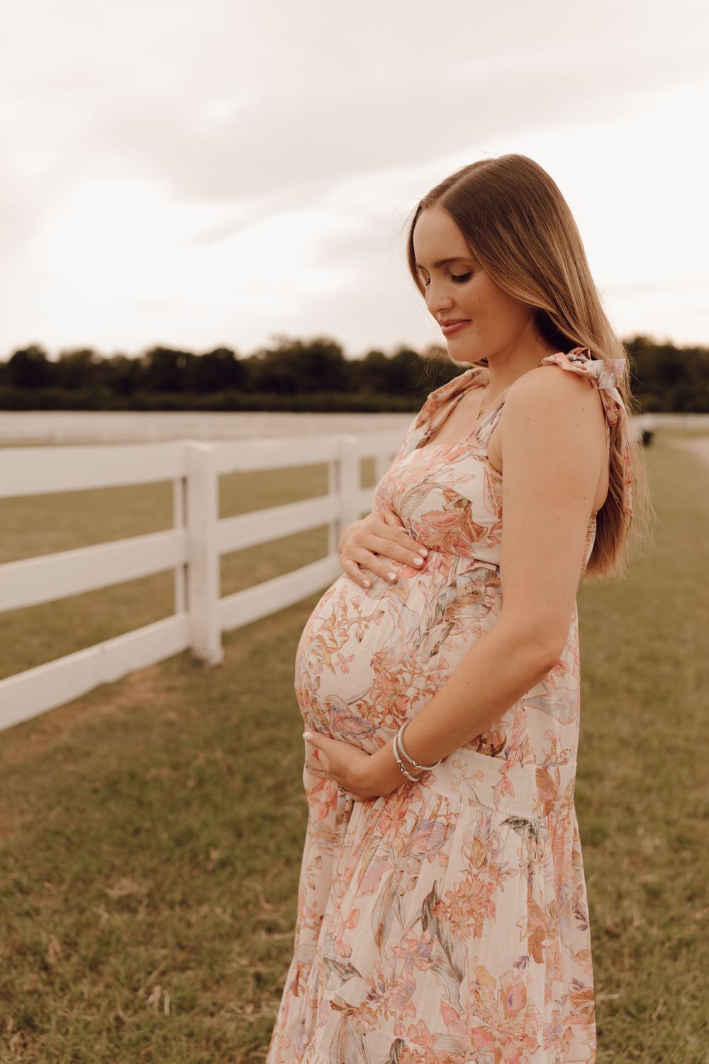Elegant maternity portrait of a woman with a glowing smile, standing in a scenic outdoor location.