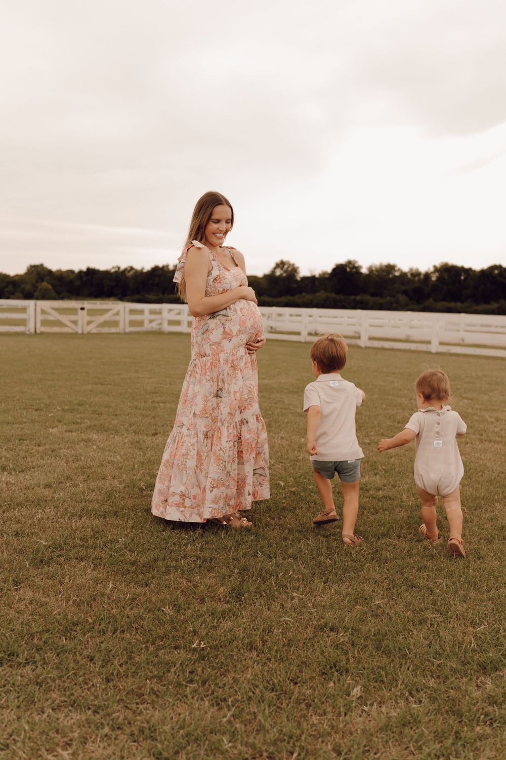 Elegant maternity portrait of a woman with a glowing smile, standing in a scenic outdoor location.