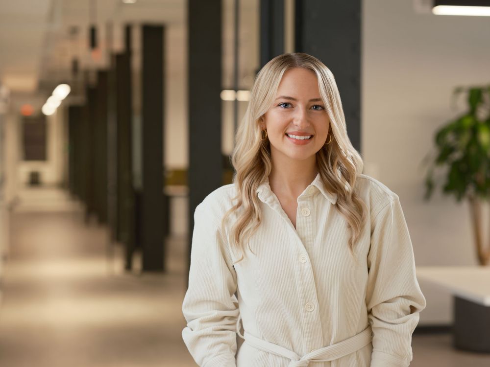 Business portrait of a smiling woman in a neutral outfit standing in a corporate hallway — captured in Boston by Khoi Ly.
