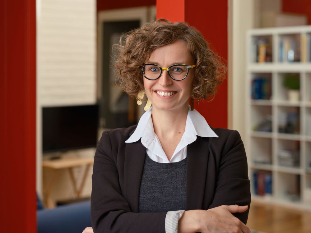 Energetic business portrait of a woman with curly hair and glasses in a library-style office — photographed in Toronto by Khoi Ly.