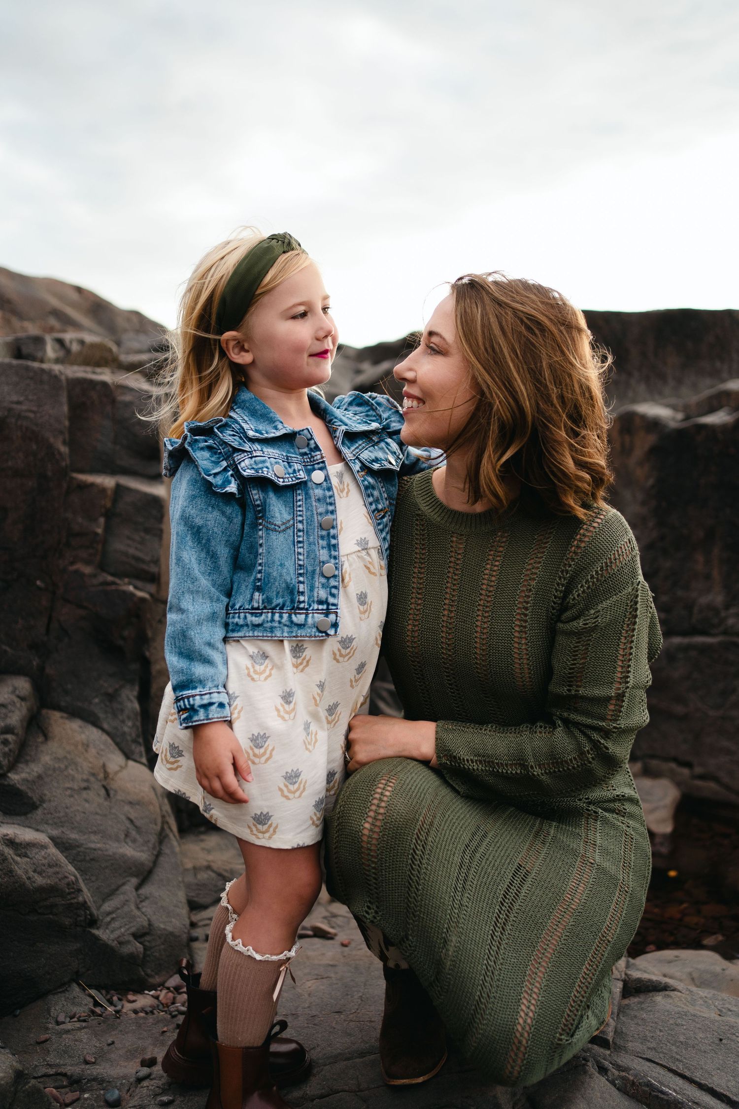 A candid moment captured on rocky terrain showing a sweet interaction between two people wearing denim and green knit dress.