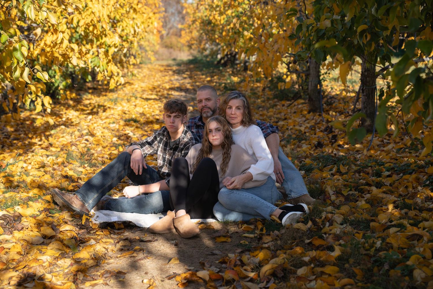 Family relaxing together on golden autumn leaves in a park setting.
