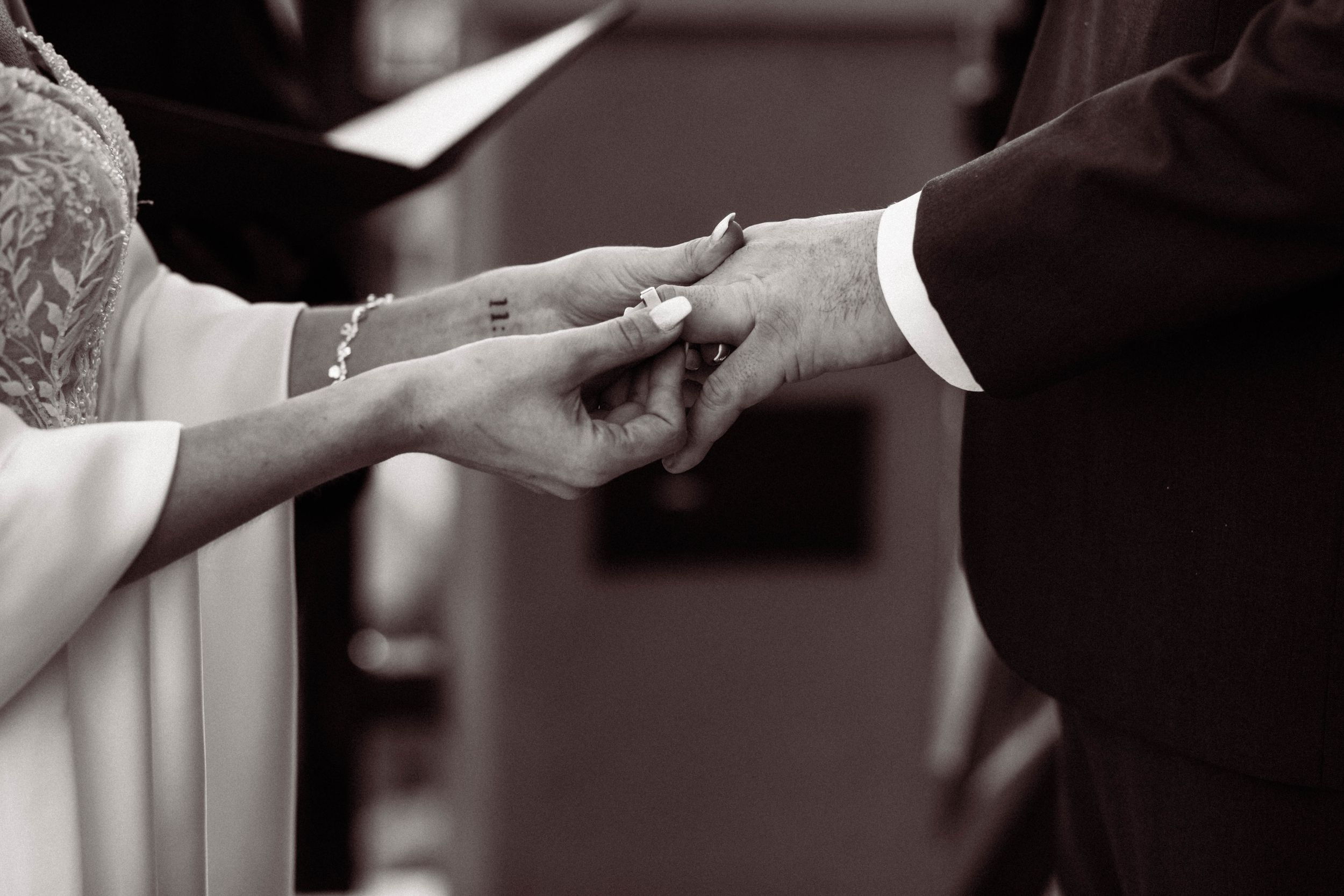 A black and white close-up photograph captures hands exchanging wedding rings during a marriage ceremony.
