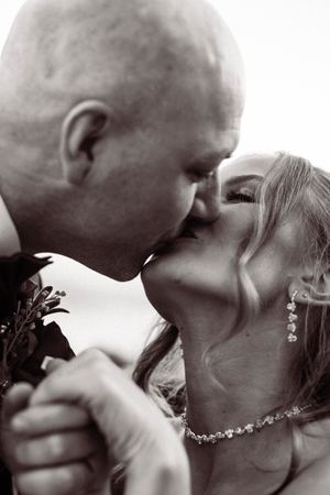 A romantic black and white close-up photograph of a tender kiss between newlyweds wearing wedding attire.