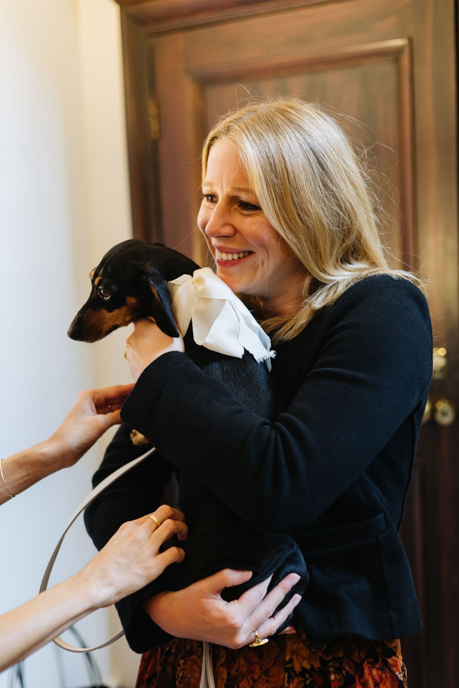 Someone wearing black holding a small dachshund puppy while smiling warmly.