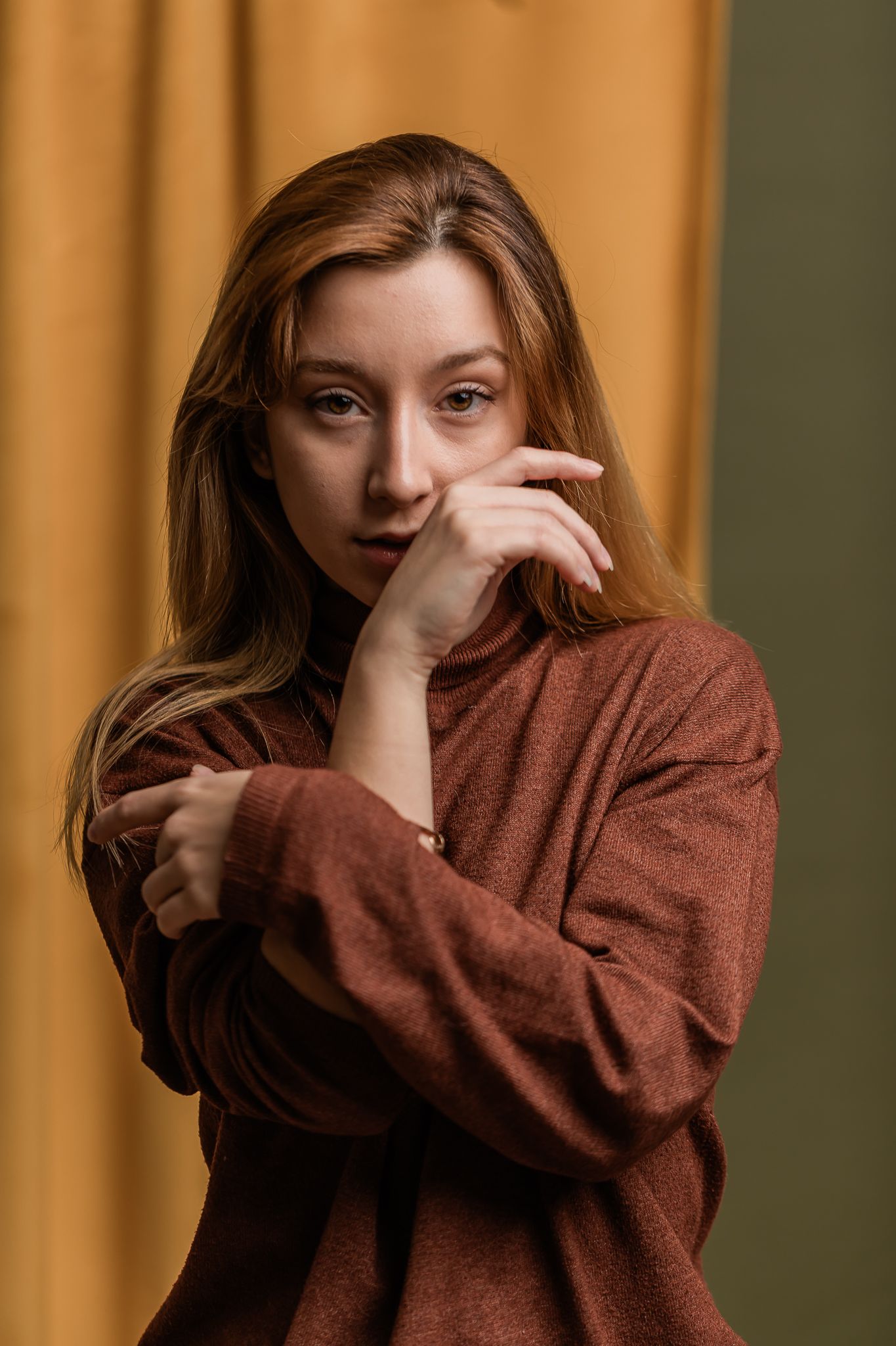 Portrait in warm tones showing subject in brown sweater against orange backdrop with contemplative pose and expression.