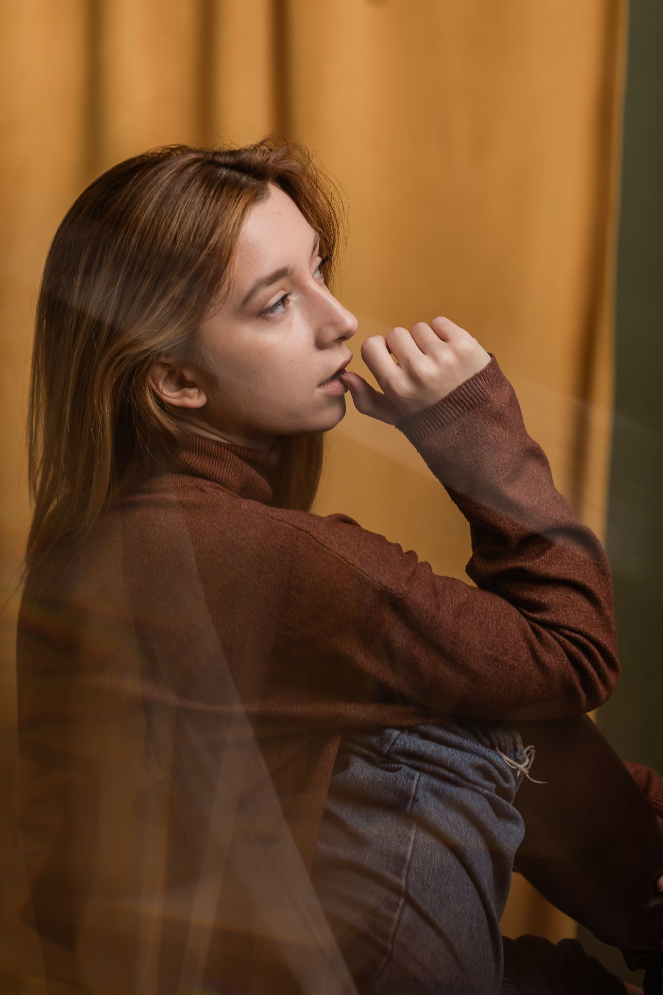 A contemplative portrait of a young woman in a brown sweater against a warm-toned background.