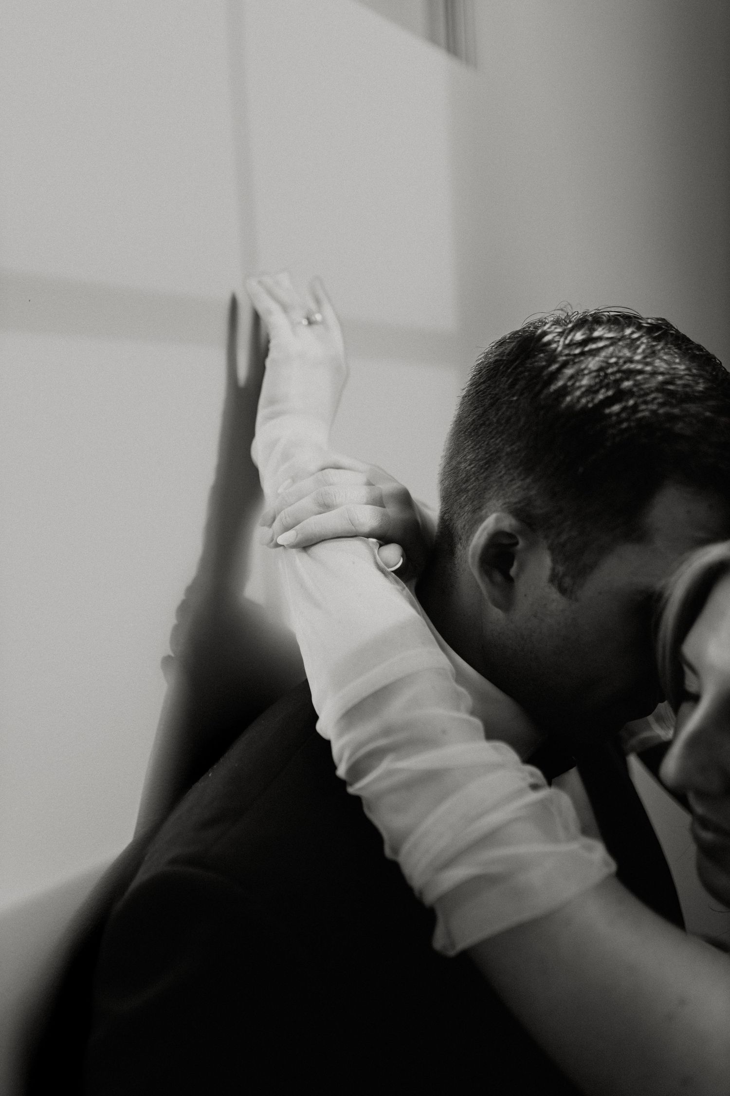 Intimate black and white photo of couple embracing against wall.