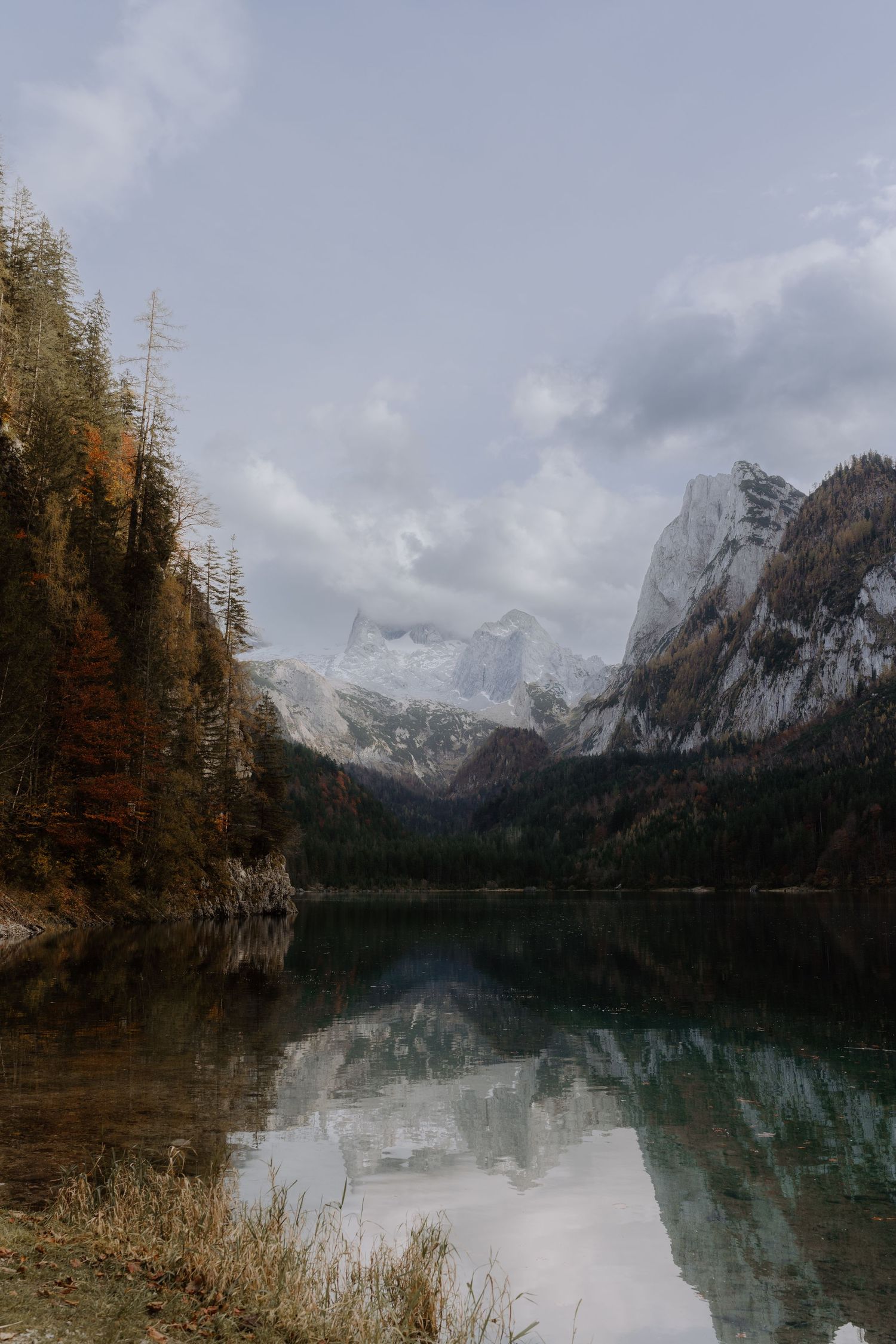 Snow-capped mountains reflect perfectly in a pristine alpine lake surrounded by autumn trees.