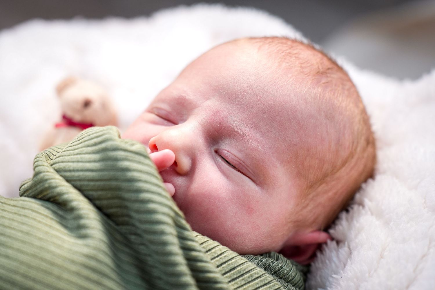 A peacefully sleeping baby in a green ribbed sweater rests on white bedding.