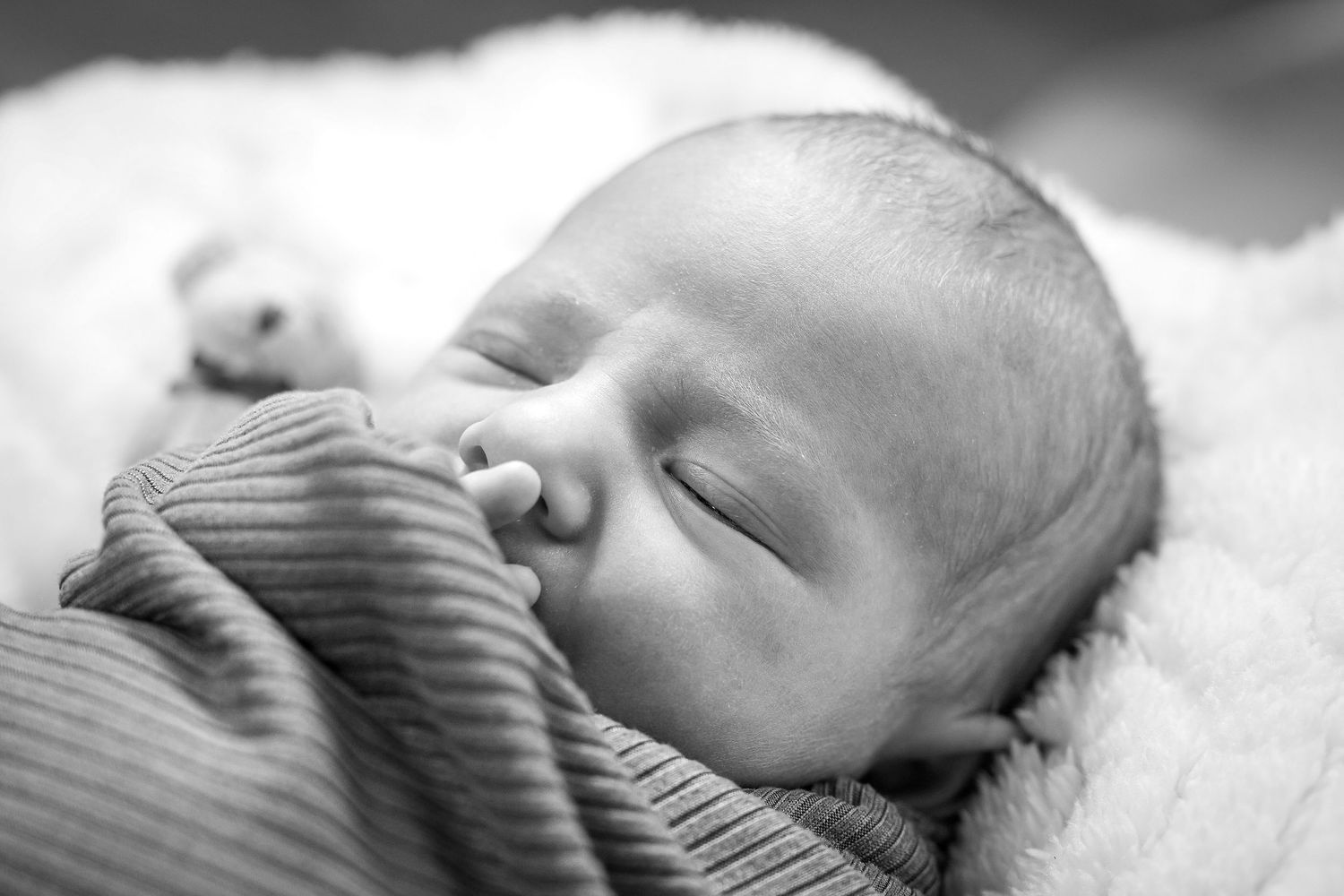 A peaceful sleeping infant rests on soft blankets in black and white.